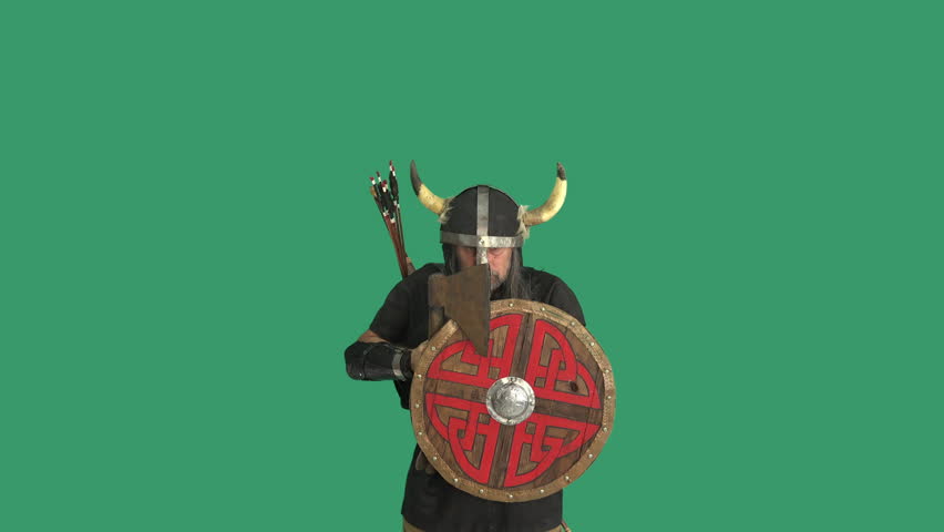 Male Viking warrior in horned helmet holding axe and round shield while posing aggressively on green screen background. Medieval Scandinavian fighter with copy space for compositing and chroma key editing