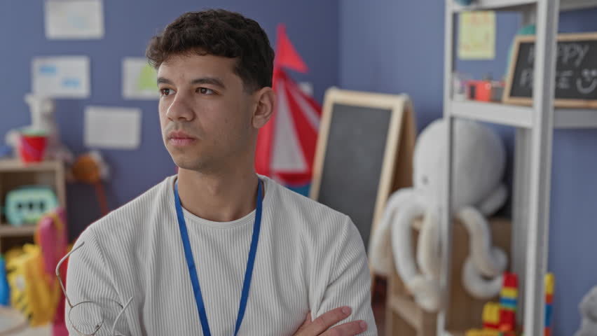 Man teacher holding glasses to mouth and arms crossed in a school building; thoughtful planning reflection.