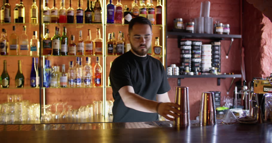 Cocktail making. Barman working. Bearded male skillfully putting ice cubes using metal scoop shaker cup in restaurant.