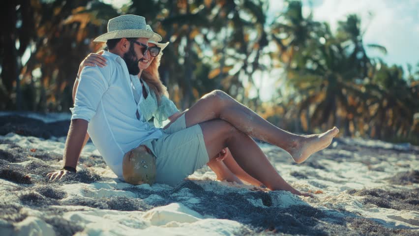 Happy Romantic Couple Relaxing On Tropical Beach Sands During Summer Vacation, Smiling Man And Woman Wearing Straw Hats And Sunglasses Sitting Together Under Palm Trees, Beautiful Young Pair Enjoying Honeymoon Travel In Paradise Resort, Cinematic Sunlit Coastal Landscape With Coconut, Joyful Relationship Expression, Serene Oceanfront Leisure Lifestyle, Tropical Getaway Destination, Tourism And Wanderlust Concept, Dreamy Holiday Mood, Authentic Connection, Summertime Bliss, Exotic Island Trip