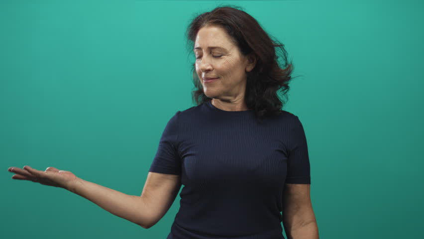 Middle age hispanic woman presents open palm gesture in studio, looking sideways as if offering something; serenity invitation.