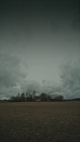 Moody Rural Landscape Under Heavy Gray Clouds - Desolate Winter Field with a Secluded Farmhouse and Silhouetted Trees