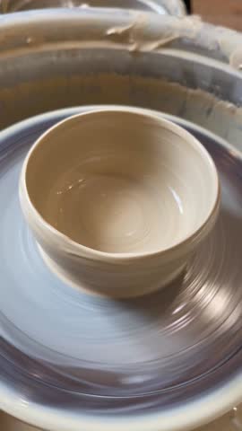 The process of shaping a clay bowl on a spinning pottery wheel in an art studio.