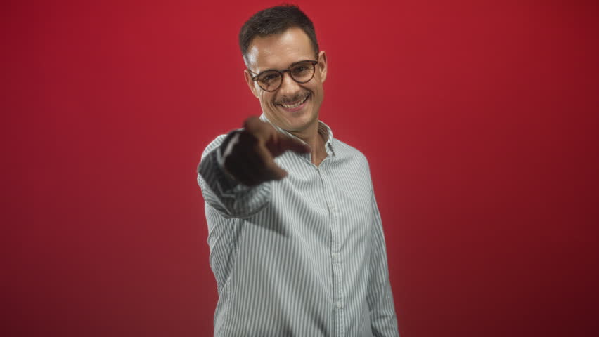 Man forming a heart with hands and smiling at camera, glasses on and striped shirt visible in a studio; warmth kindness.