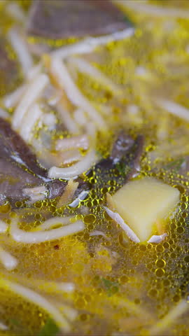 Soup with noodles. Steaming bowl of mushroom noodle soup with toppings and oil droplets. Detailed view of simmering mushroom noodle soup garnished with herbs and oil