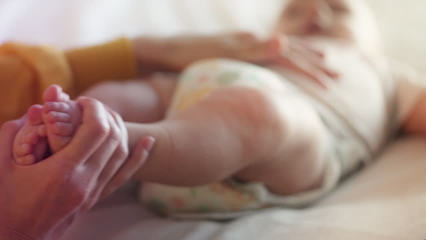 Mother playing with newborn daughter, touching tiny baby feet affectionately