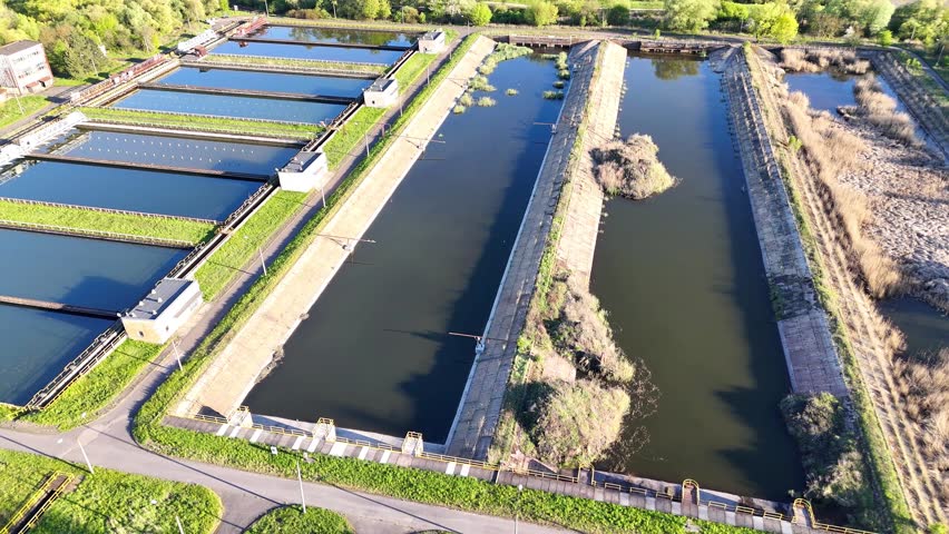 Aerial view of rectangular water treatment ponds with green vegetation along the edges, showcasing multiple parallel channels and varying water levels in a natural landscape