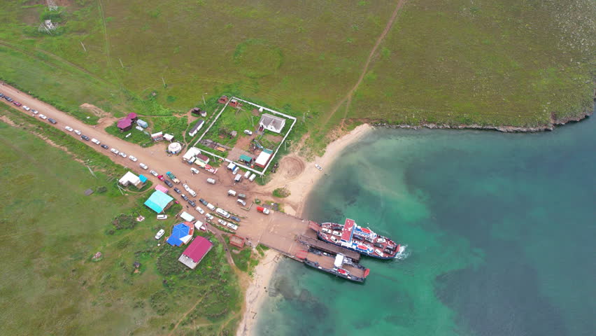 An aerial view of Lake Baikal. Cars and tourists are loading onto ferries at the Olkhon Island pier. A long line of cars. Summer travel.