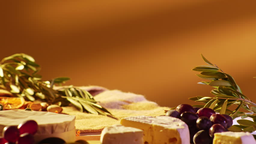Hand placing a slice of crusty baguette on a rustic wooden board with camembert cheese grapes and olive branches in warm golden light