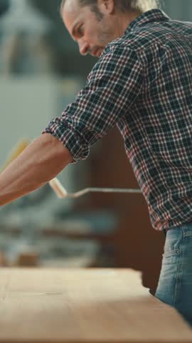 Male carpenter pouring white glue in a line on a wooden plank inside a workshop