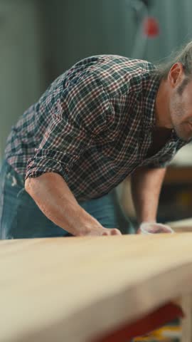 Concentrated man carefully applying a protective coat of varnish on a wooden plank in his workshop