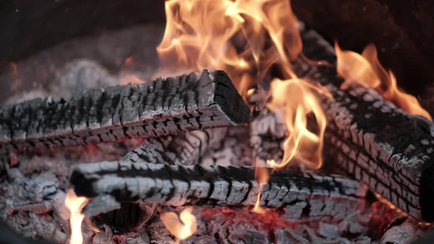 Close-up view of burning firewood logs in a campfire with bright orange flames and glowing embers