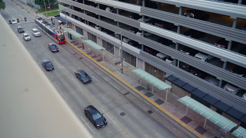 Houston METRORail light rail train traveling through Downtown Houston street beside parking garage and city traffic during daytime, showcasing public transportation infrastructure in Houston, Texas, U
