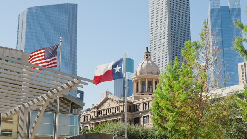 Texas and American flags waving in front of Houston City Hall with Downtown Houston skyline and modern skyscrapers in the background on a sunny day in Houston, Texas, USA.