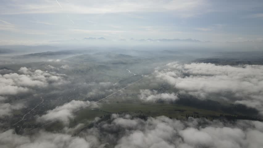 High altitude aerial view looking down at a rural valley through scattered clouds with mountain ranges on the horizon
