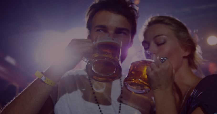 Male-female pair toasting mugs, sparkle overlay sweeping, camera pulling back revealing club. Couple, nightlife, neon, bokeh, amber, glow, crowd