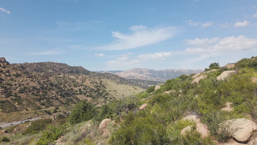Aerial flyover of Santa Susana Pass State Historic Park overlooking the San Fernando Valley, with rugged hills, rocky terrain and sweeping California mountain scenery under blue skies.