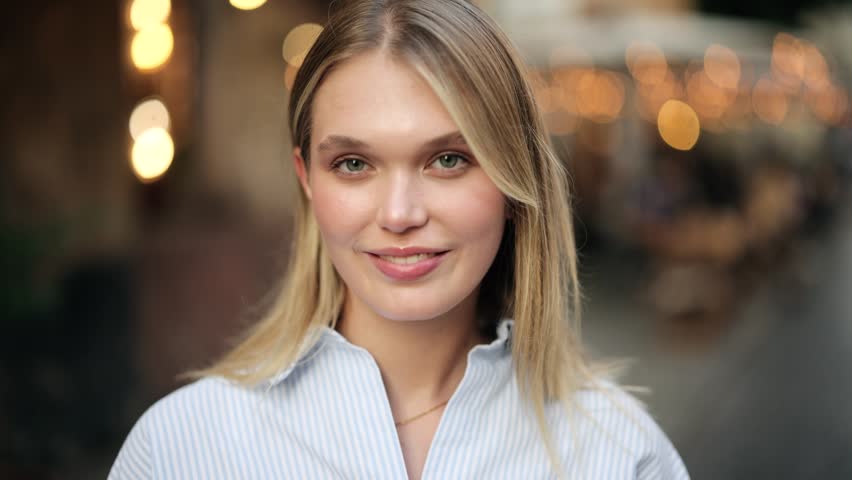 Close-up portrait of beautiful young blonde woman smiling and looking at camera on city street