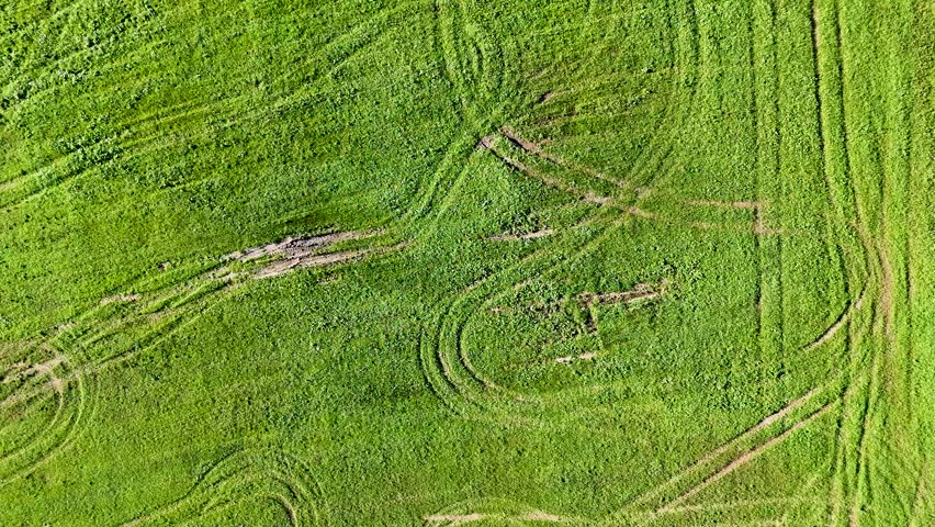 Aerial drone footage flying over a lush green field marked with intricate tractor tire tracks. A beautiful rural landscape with grass