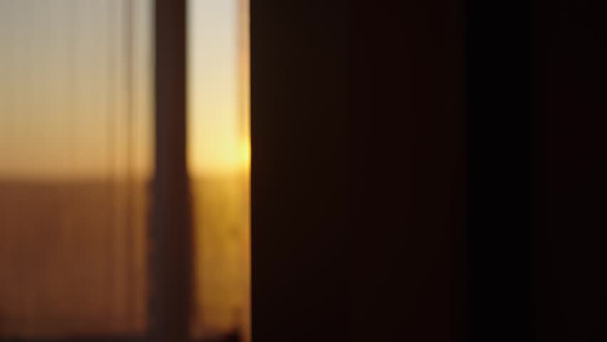 Bright morning sunbeam peaking through a window with a sheer curtain, illuminating a dim room with its warm, golden rays and creating a beautiful, atmospheric lens flare effect