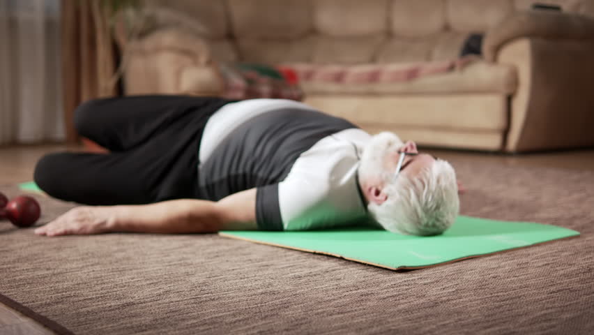 Old man in excellent physical condition does morning exercises on a mat at home