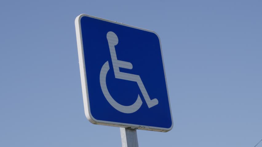 Low angle close-up of a blue handicapped parking sign shot in daylight with clear sky. Crisp, static composition ideal for accessibility themes.