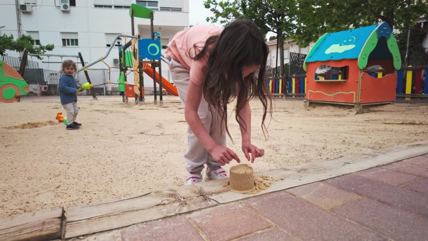 Young Children Play Happily in a Sandy Playground, Making and Breaking Sandcastles