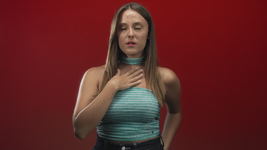 Woman with hand on chest looking sideways in studio wearing teal tube top and choker; surprise hesitation.