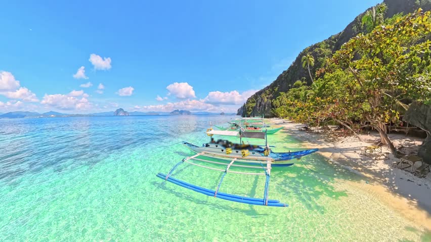 Entalula Beach, El Nido: traditional bangka boats moored in crystal turquoise water beside white sand, dramatic limestone cliffs and lush tropical vegetation under blue skies of Palawan, Philippines