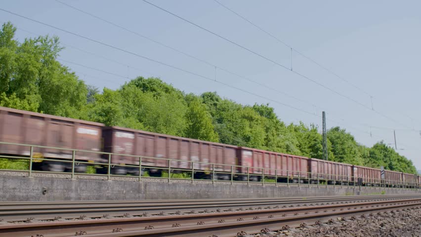 Freight train moves along railway tracks beside green trees on a sunny day