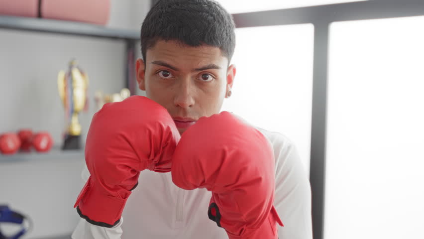 Man throwing a jab with red boxing gloves in a training studio with trophies on shelf; determination.