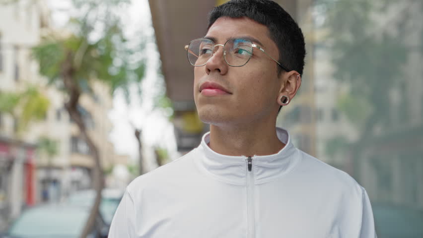 Man wearing glasses and a white zip jacket smiling while looking up on a city street; optimism wonder.