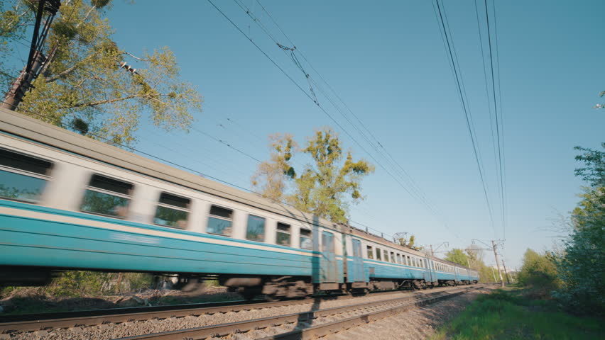 Blue Passenger Train Moving Fast Along Railway Track | Suburban Electric Train in Motion with Motion Blur | Ultra-Wide Side View on Sunny Spring Day