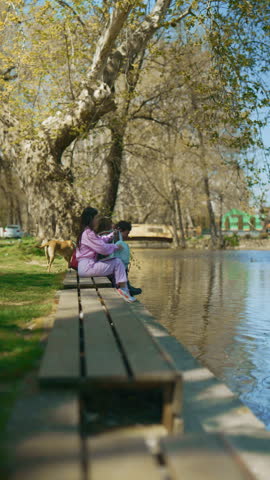 Young students are learning together on a park bench by a river. They enjoy a peaceful outdoor study session.