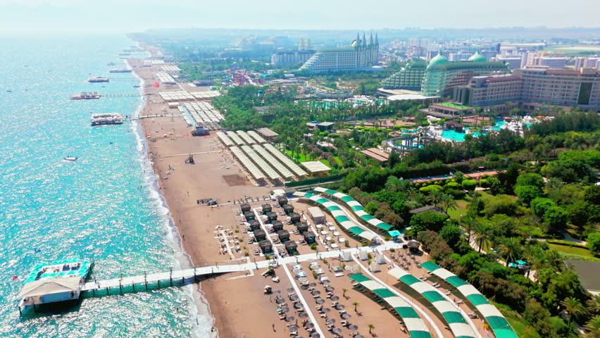 Drone aerial of beach coastline in Turkey. Wide sandy shore with hotels and city buildings along the waterfront.