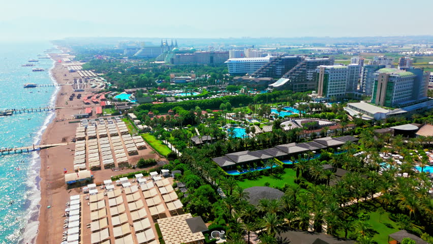 Drone aerial of long sandy beach in Turkey. Beachfront promenade and coastal city hotels along the shore.