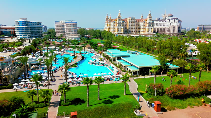 Drone aerial of resort hotel district in Turkey. Pool complex and landscaped gardens near the coast with people relaxing on their holidays in Antalya.