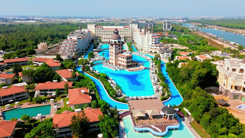 Drone aerial of a 5-star hotel and resort in Antalya, Turkey. Luxury hotel complex with long central pool and palm-lined grounds.