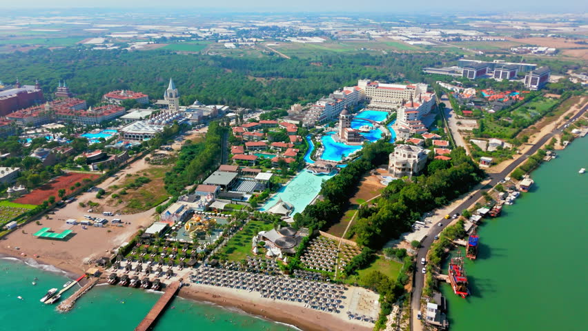 Drone aerial of a 5-star hotel and resort in Antalya, Turkey. Coastal resort area with luxury hotels, gardens, and nearby waterfront.