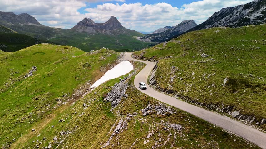Aerial drone view of the mountains in Durmitor National Park, Montenegro. A car drives along a scenic mountain road through the forest and towering mountains. Beautiful mountain landscape.	
