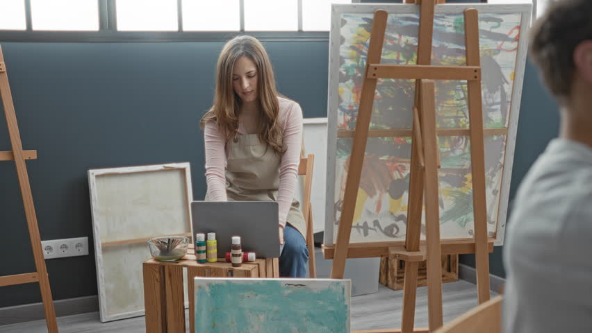 Man holds brush to canvas, hand on palette and wearing apron at easel in studio; concentration collaboration.