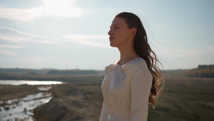 Young girl in a white dress stands under a bright open sky. Concept of a female face.