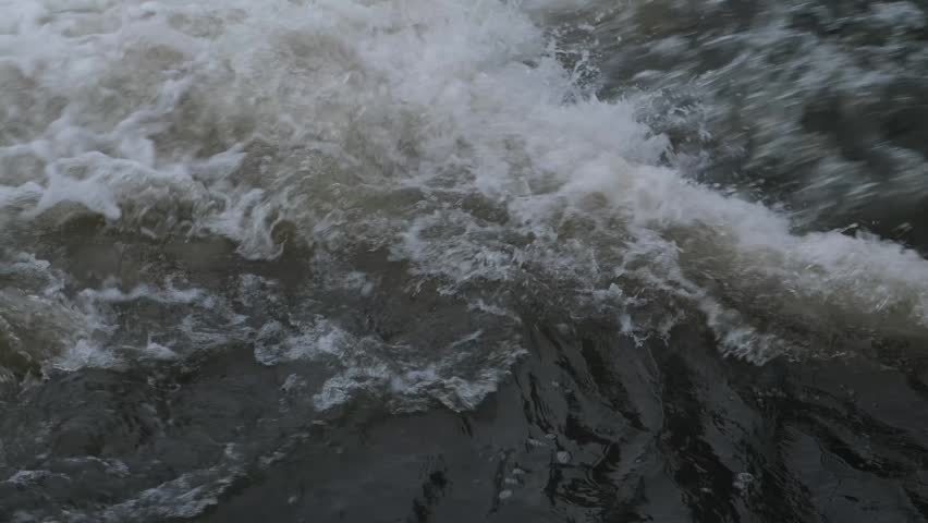 Powerful river flow with churning white foam and splashes. Close up of fast water on mountain river rapids