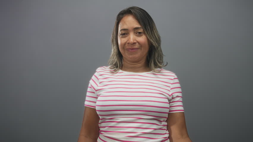 Woman covering face with hand and peeking through fingers in studio wearing pink striped t shirt; shyness privacy.