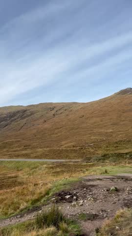 Vertical slow pan of the Three Sisters mountains in Glencoe, Scottish Highlands, featuring the dramatic autumnal colors and rugged peaks of the Glencoe valley in autumn.