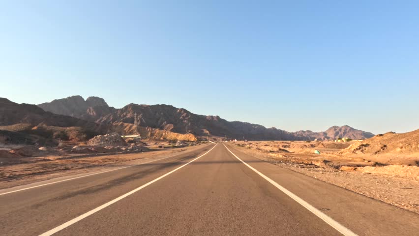 Car driving on straight desert highway through open mountain landscape