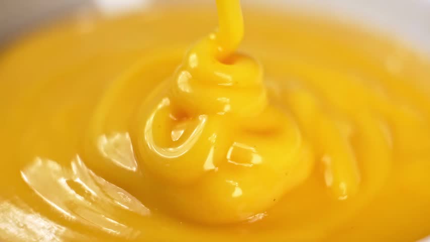 Thick yellow mustard sauce pouring and swirling in an extreme macro close up view