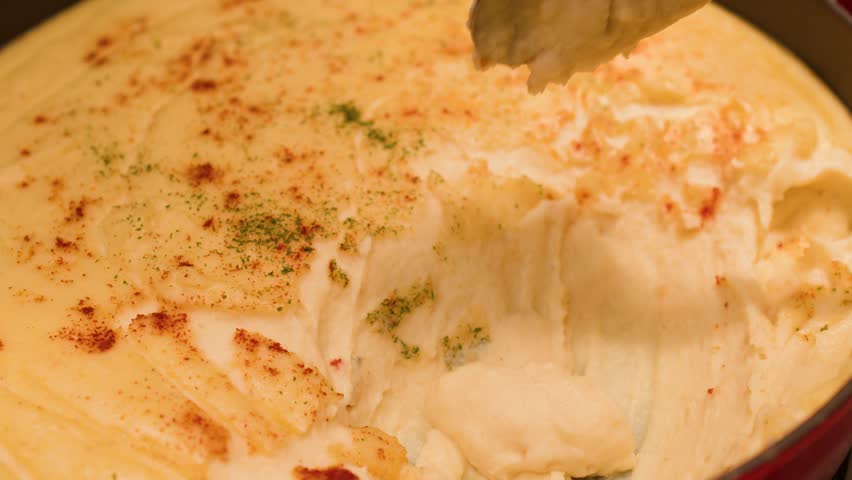 Close-up shot of a metal spoon scooping creamy mashed potatoes topped with paprika and herbs