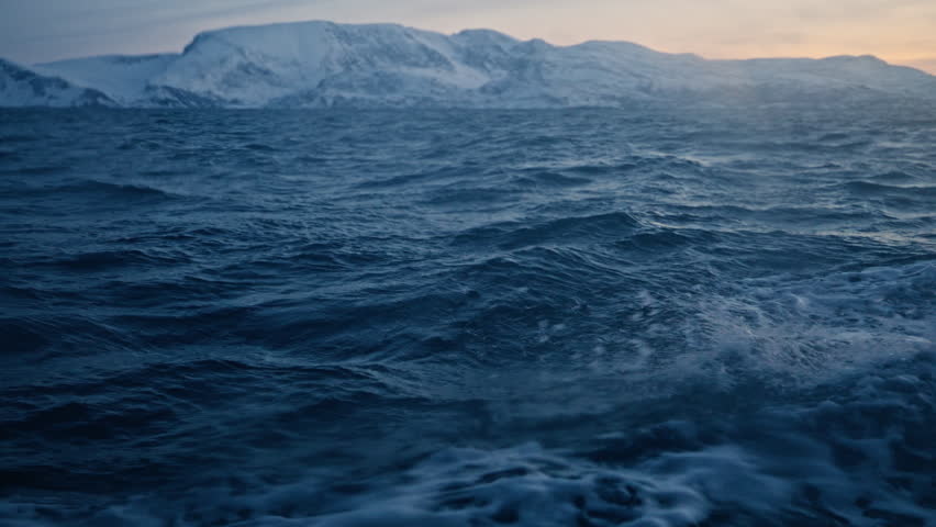 Choppy Arctic Ocean water with large snow covered Norway mountains rising beyond horizon