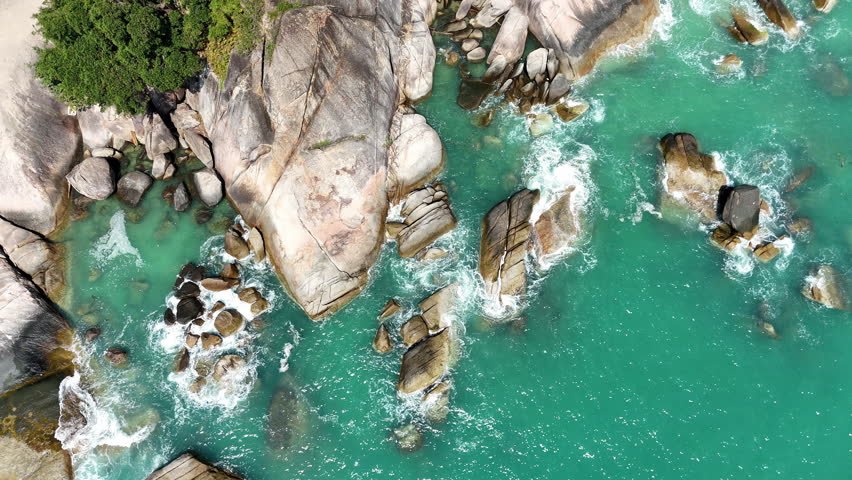Aerial drone view of ocean waves breaking against large coastal rocks in turquoise water in Thailand